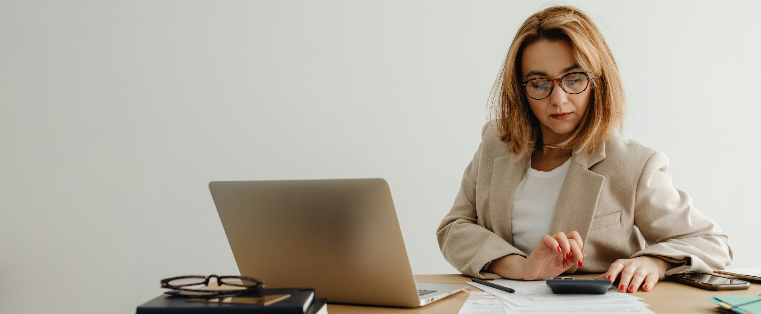 woman using a calculator at her desk which has a laptop and paperwork on it